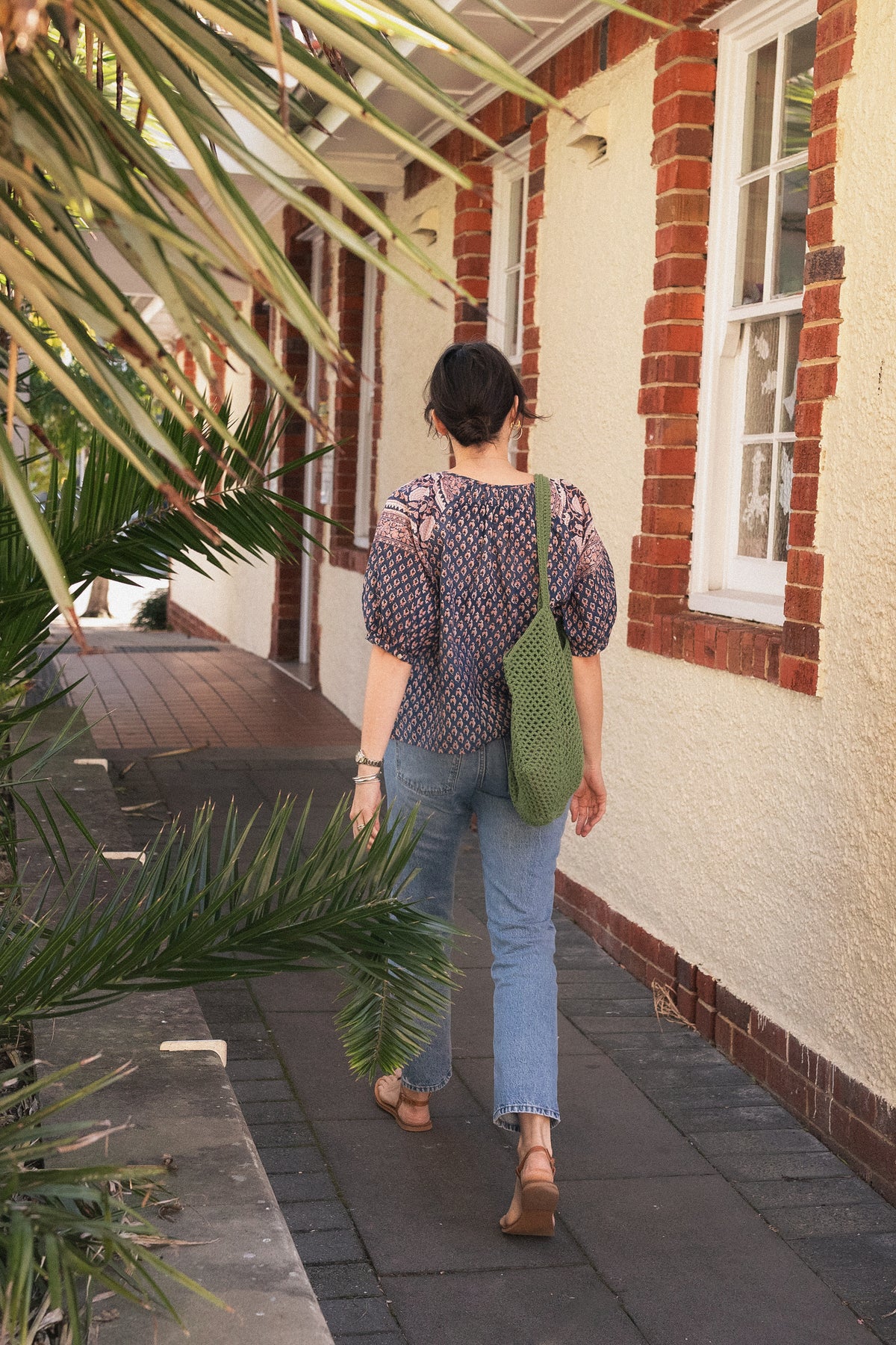 Woman walking wearing the Lisette navy hand block printed blouse with jeans and green crochet tote bag.