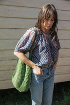 Woman wearing the Lisette navy hand block printed blouse with jeans and green crochet tote bag.
