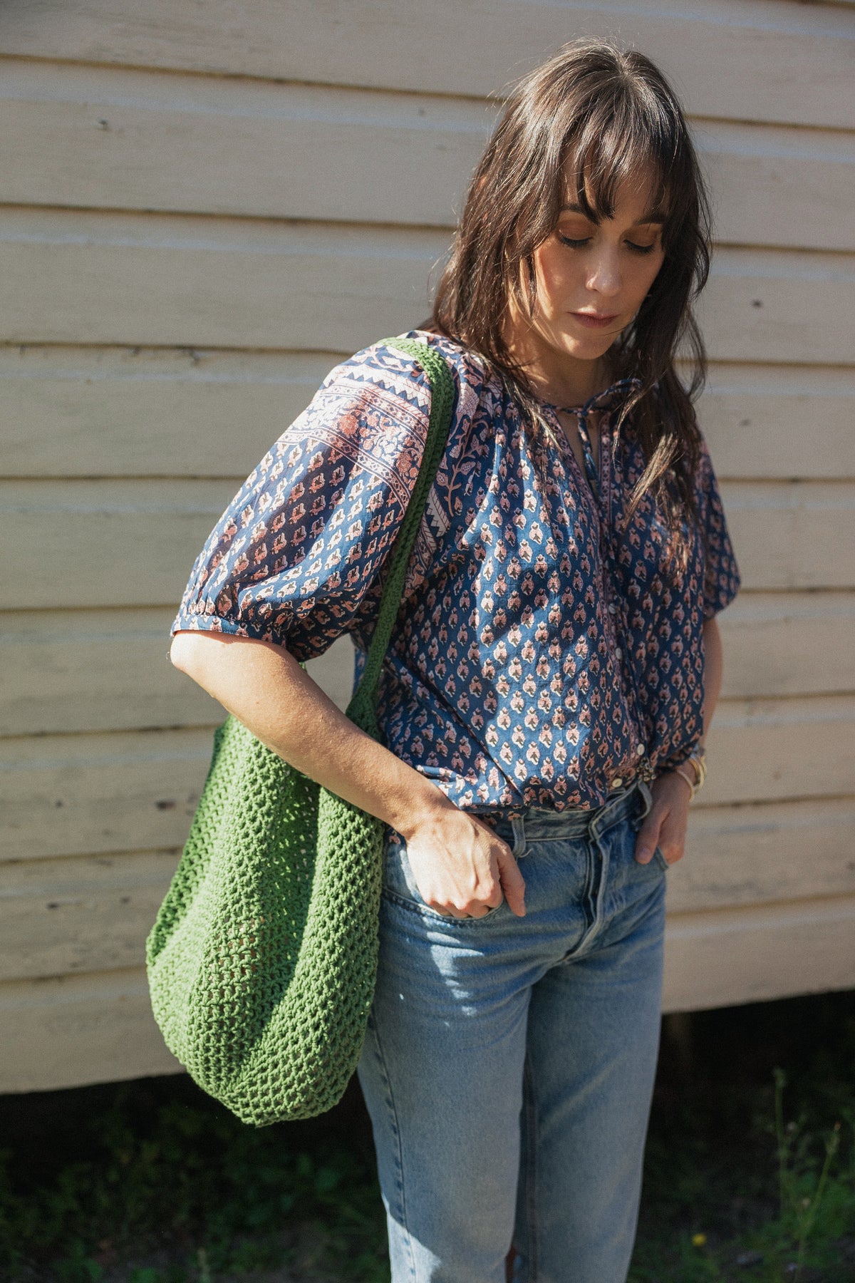 Woman wearing the Lisette navy hand block printed blouse with jeans and green crochet tote bag.