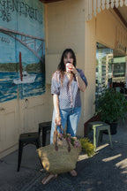 Woman wearing the Lisette navy hand block printed blouse with jeans and carrying basket of pink and yellow flowers.