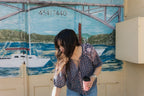 Woman in front of seaside mural wearing the Lisette navy hand block printed blouse with jeans.