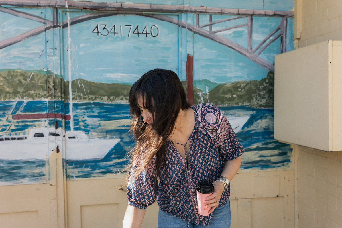 Woman in front of seaside mural wearing the Lisette navy hand block printed blouse with jeans.