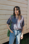 Woman wearing the Lisette navy hand block printed blouse with light blue jeans and a green crochet tote bag.