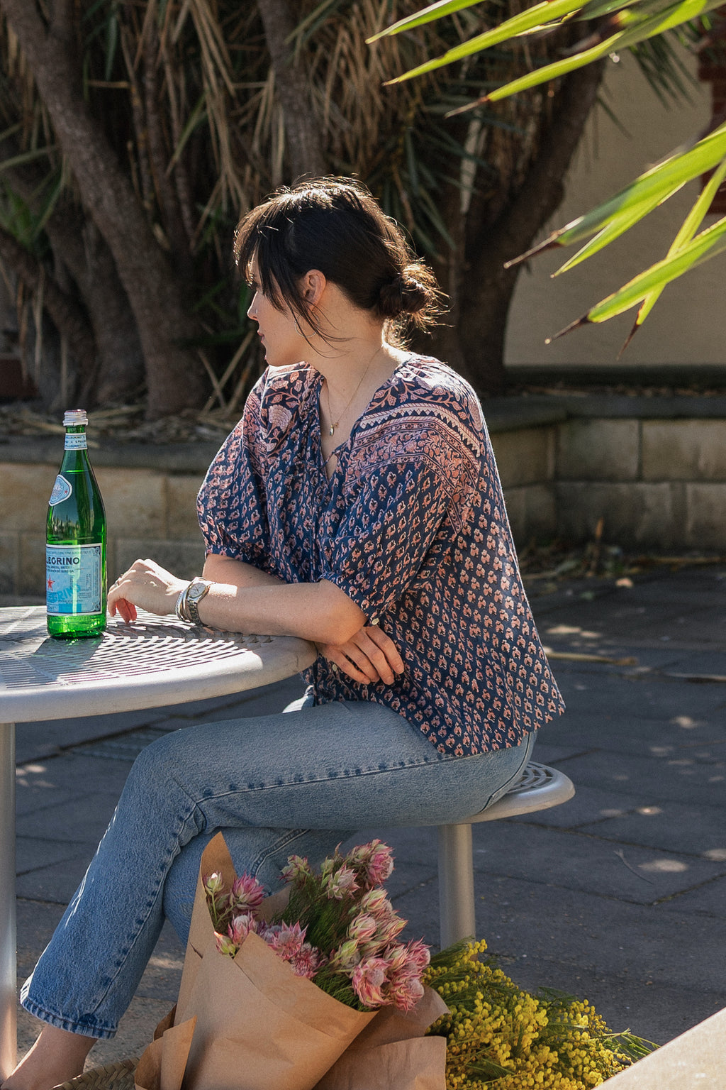 Woman sitting wearing the Lisette navy hand block printed blouse with jeans, with basket full of pink and yellow flowers.