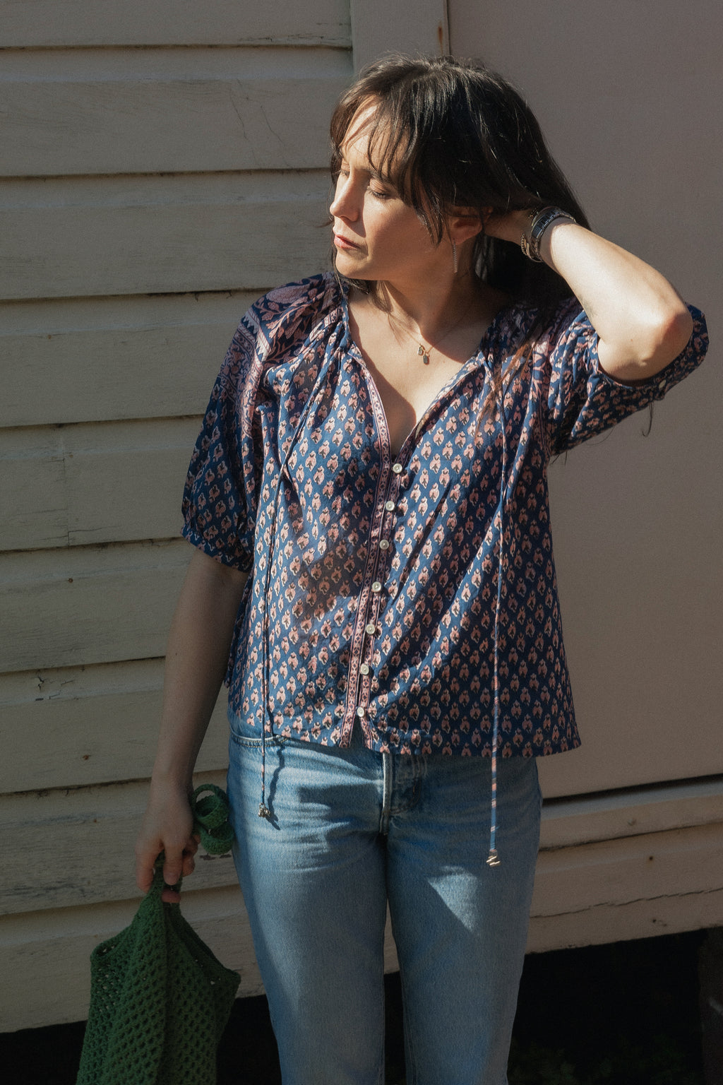 Woman wearing the Lisette navy hand block printed blouse with jeans and a green crochet bag