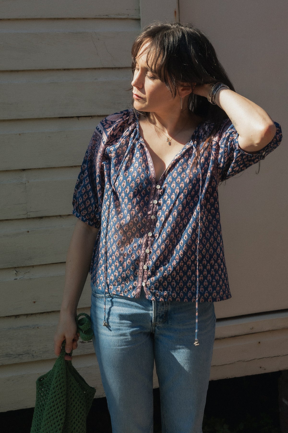 Woman wearing the Lisette navy hand block printed blouse with jeans and a green crochet bag
