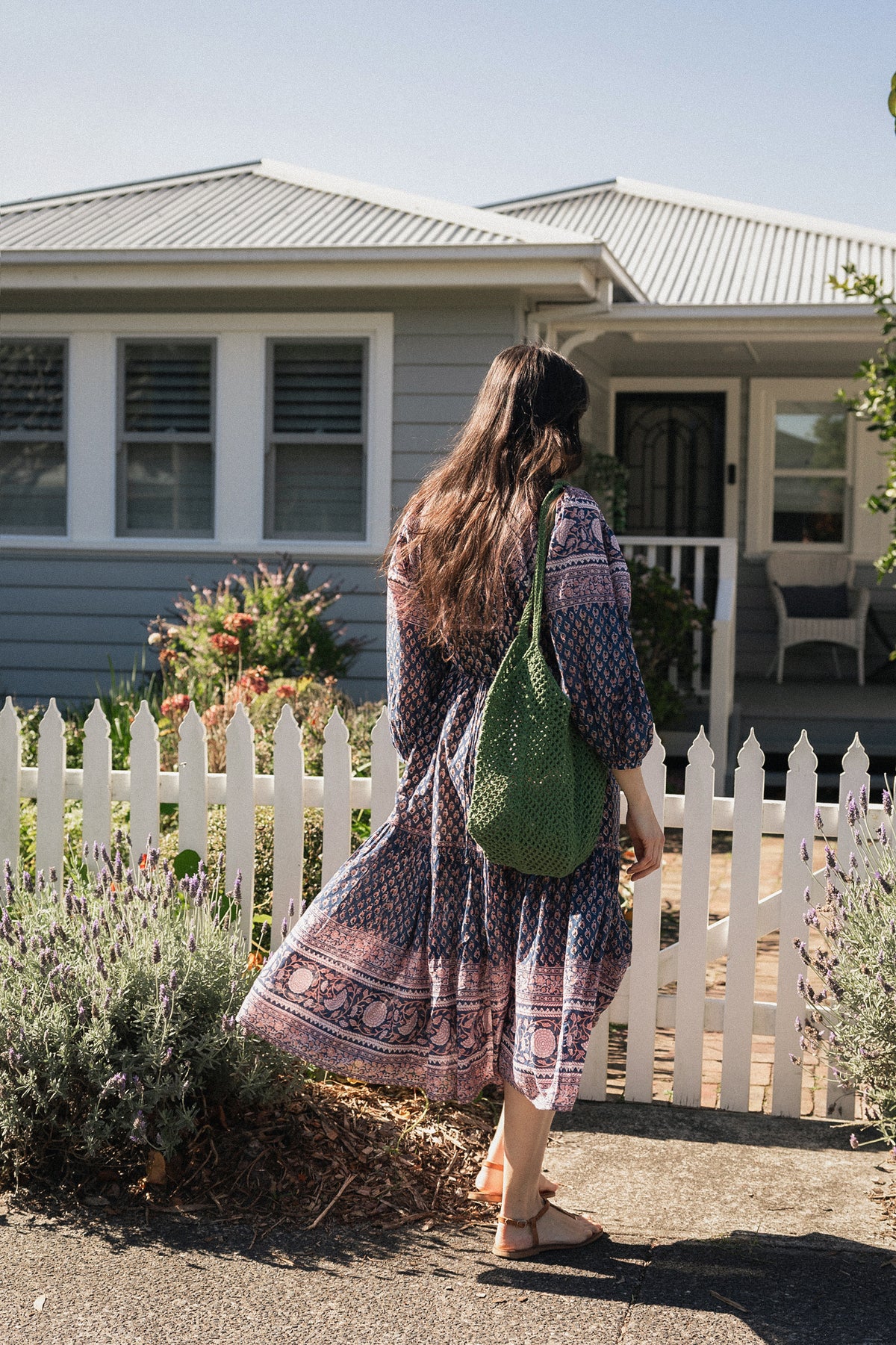 Woman in front white picket fence wearing the Lisette Midi Dress, a navy and soft nude hand block print cotton midi dress.