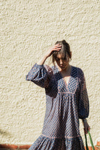 Woman against wall in sun wearing the Lisette Midi Dress, a navy and soft nude hand block print cotton midi dress.