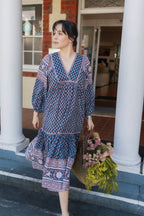 Woman walking with basket with yellow and pink flowers  wearing the Lisette Midi Dress, a navy and soft nude hand block print cotton midi dress.