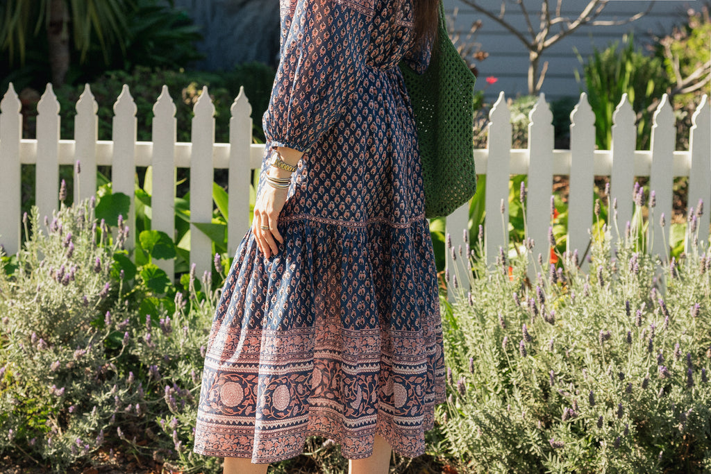 Woman in front white picket fence wearing the Lisette Midi Dress, a navy and soft nude hand block print cotton midi dress.